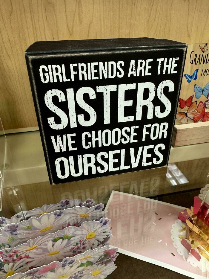 Black sign with white text saying girlfriends are the sisters we choose for ourselves, in a funny and awkward moment setting