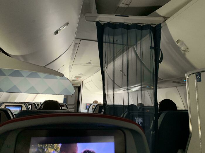 Airplane cabin interior with passengers and a dark curtain partially blocking the aisle in an awkward moment.