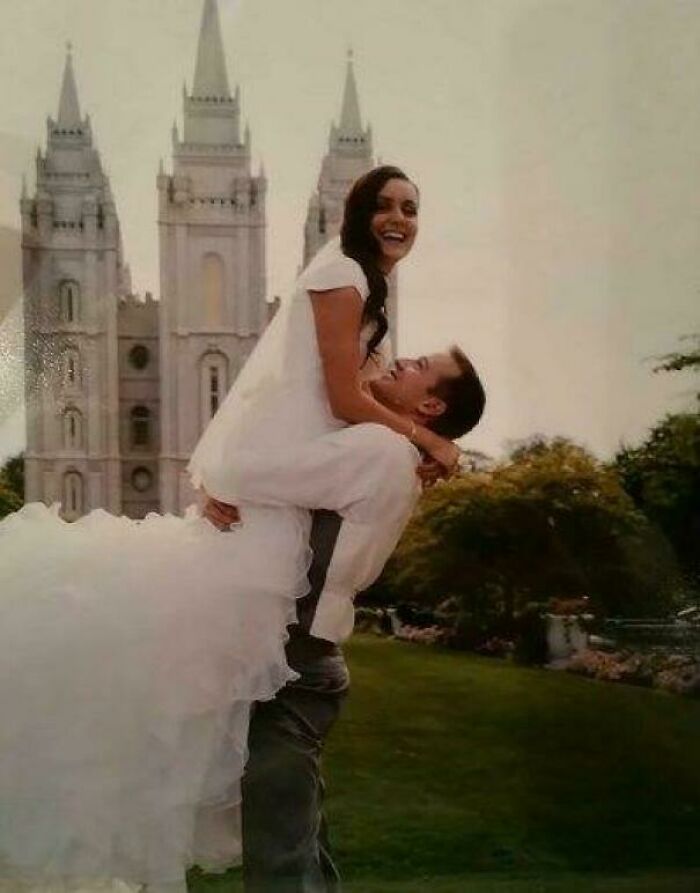 Couple in white poses playfully in front of a grand cathedral, creating a seriously confusing optical illusion.