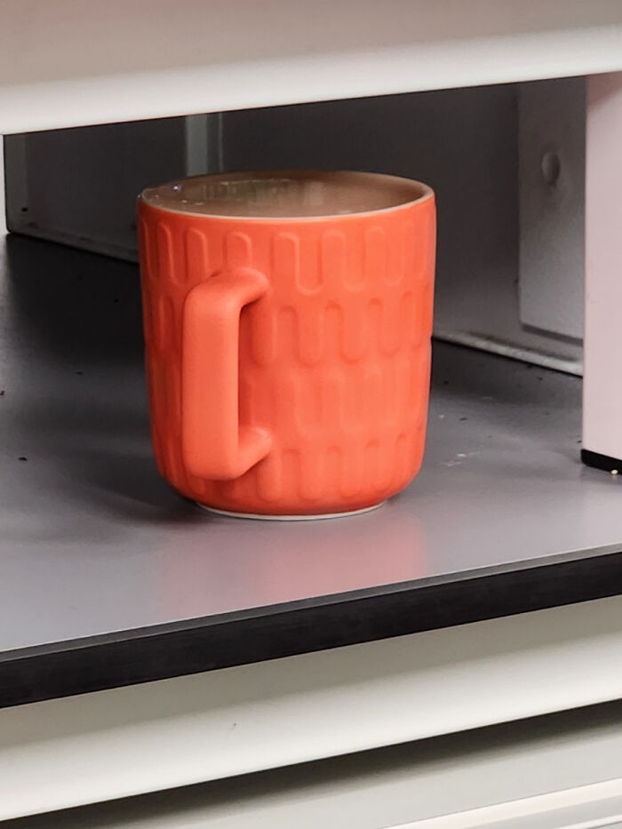 Orange mug with confusing handle placement, requiring a double take on a shelf.