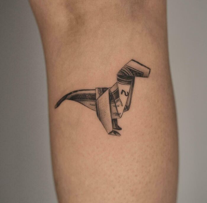 Origami dinosaur tattoo, realistic and intricately designed on forearm skin.