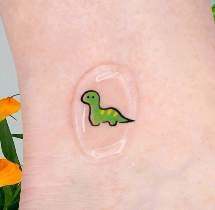 Simple green cartoon dinosaur tattoo on skin with clear protective cover.
