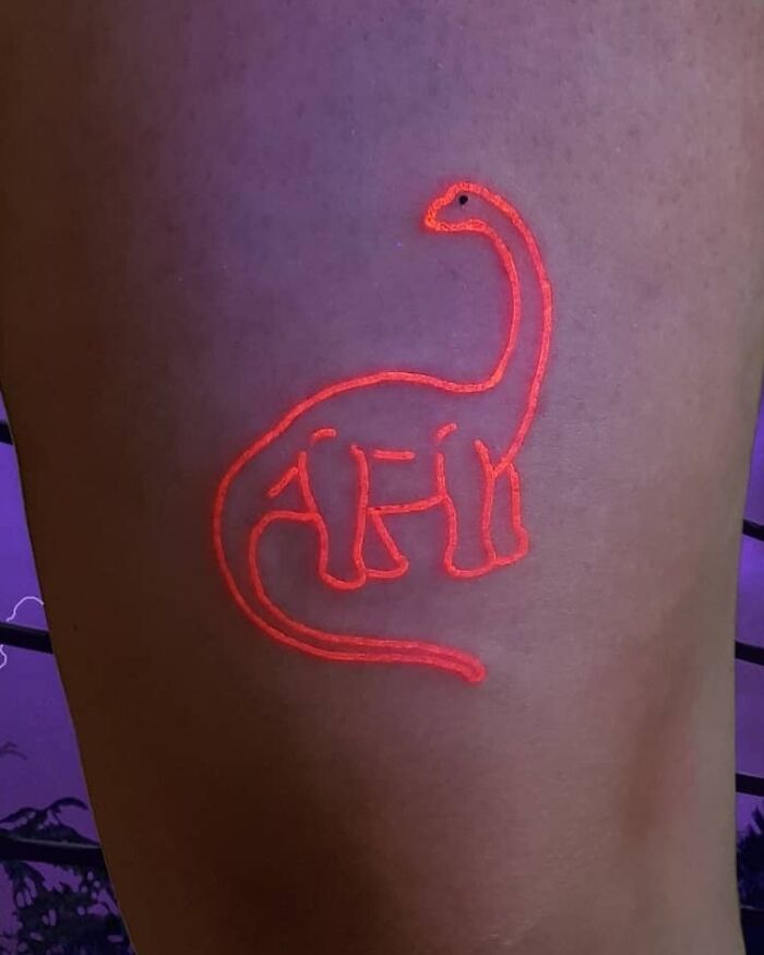 Neon orange dinosaur tattoo on thigh, showcasing a unique and creative design.