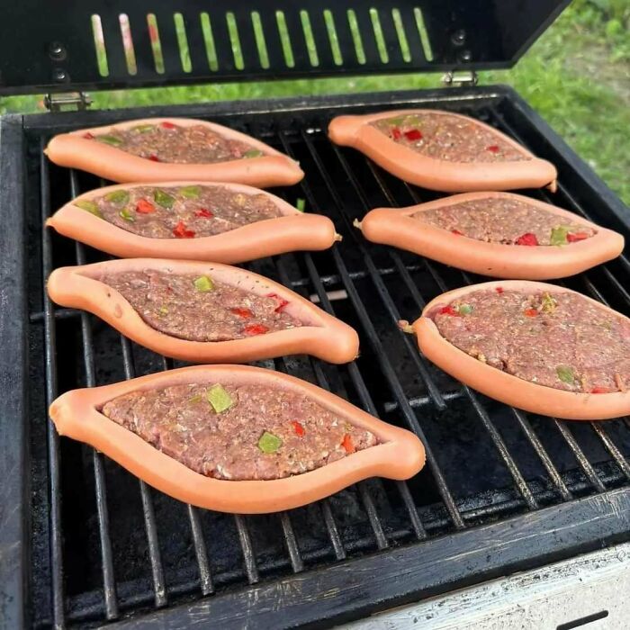 Hot dogs split and filled with meat and peppers cooking on a grill, showcasing a creative and unusual dish idea.