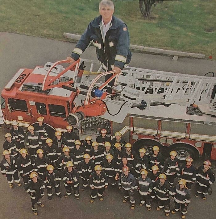 A firefighter standing on a fire truck ladder appears giant compared to the group of firefighters below, creating a confusing illusion.