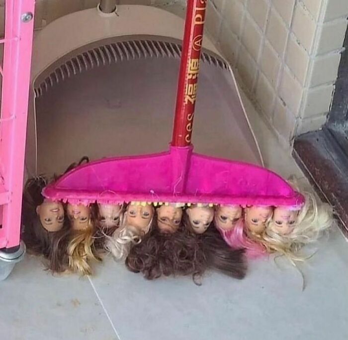 Broom sweeping a floor with multiple doll heads attached, creating a random and unusual photo scene.