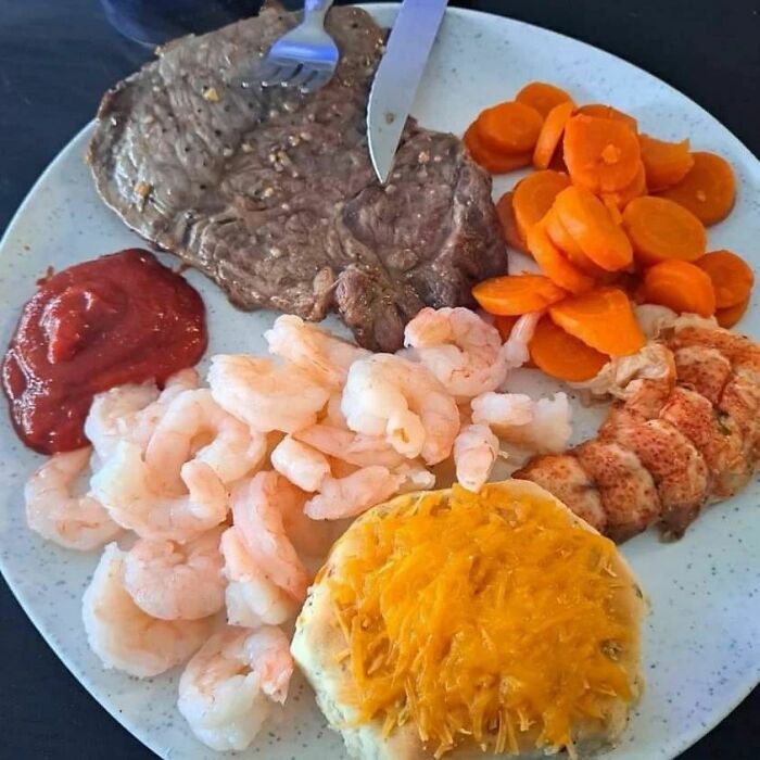 Unappetizing plate with shrimp, steak, carrots, and a cheese-topped bun, highlighting a cooking fail.