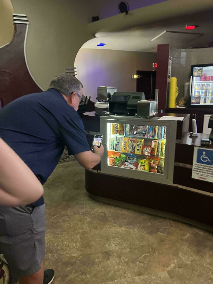 A man taking a photo of a display case filled with snacks; a confusing pic needing a second look.