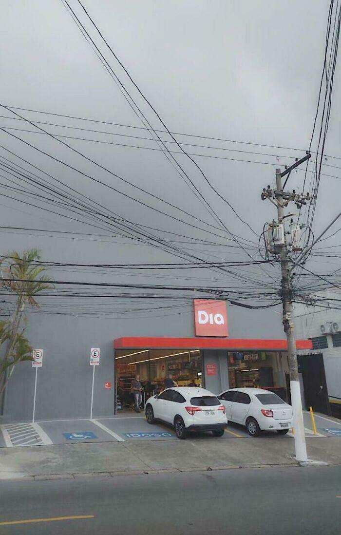 Confusing image of power lines tangled above a Dia store entrance in a parking lot.