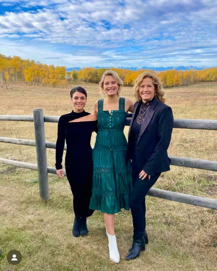 Three people standing in a field, with vibrant autumn trees, posing for a seriously confusing photo.