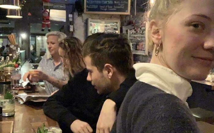 Confusing pic: a woman smiles at the camera, her shoulder blending with a man's head in a bar setting.