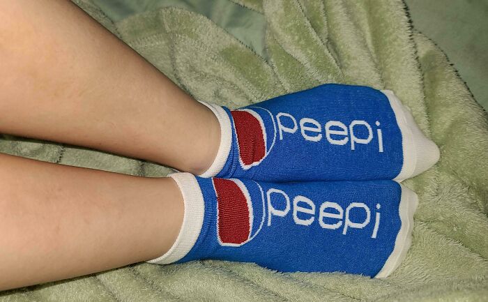 Feet wearing blue socks with a funny rip-off logo resembling a well-known soda brand in a casual setting.