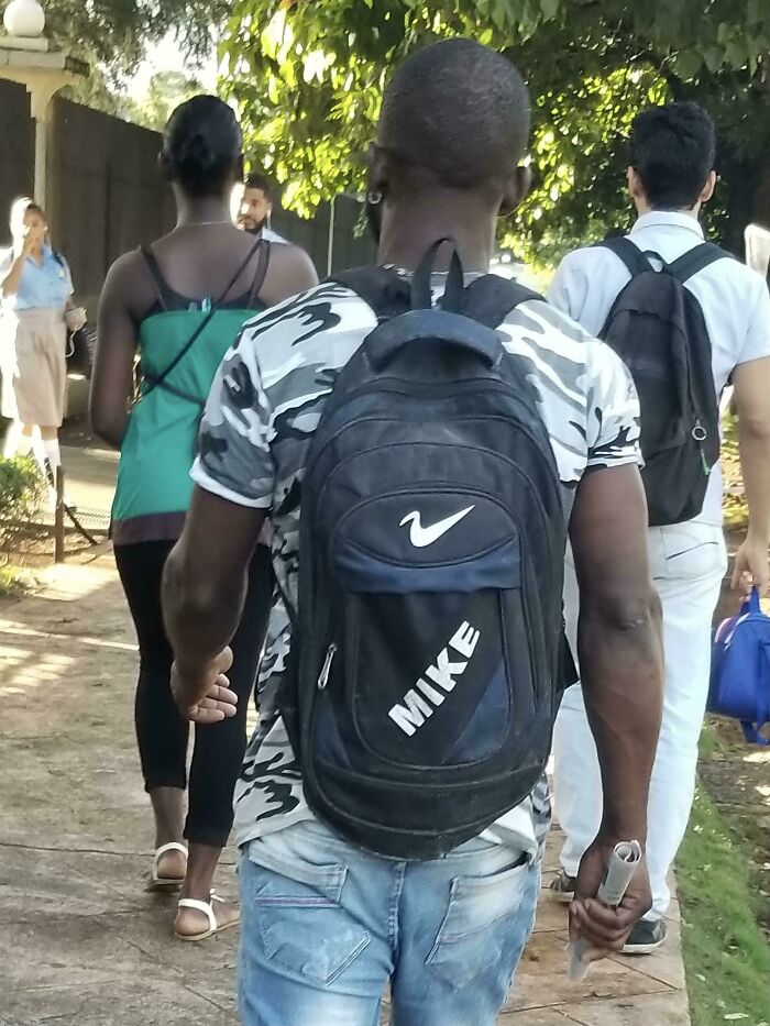 Person walking with a backpack labeled Mike featuring a fake logo, illustrating hilariously bad rip-offs of well-known brands.