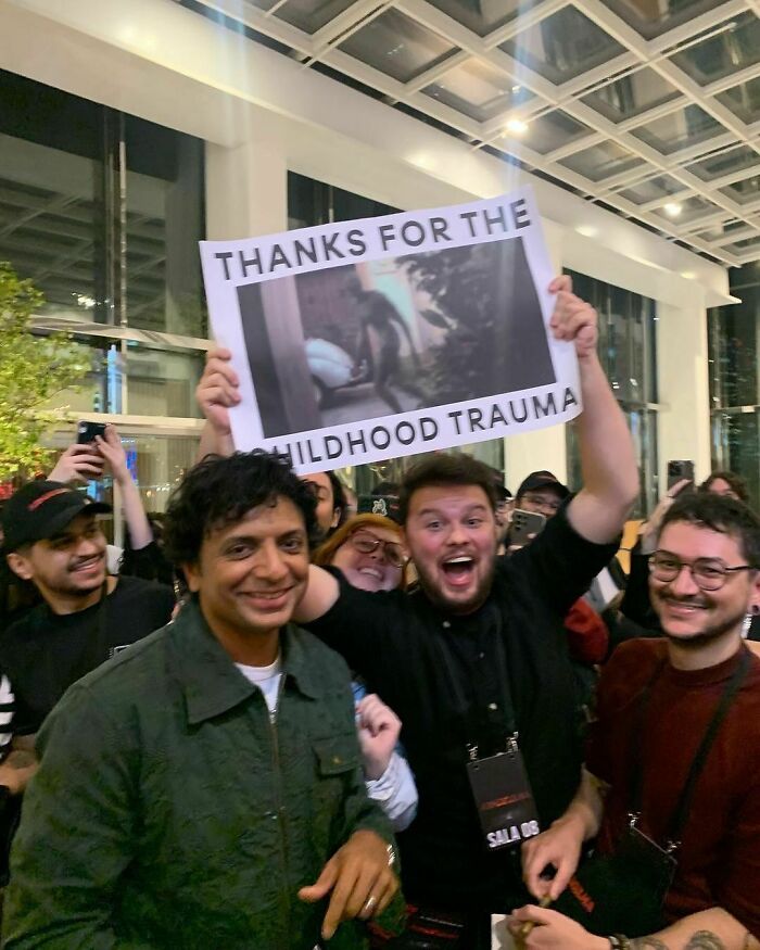 Group of people holding a childhood trauma meme sign, evoking nostalgia for Tamagotchis and VHS tapes.