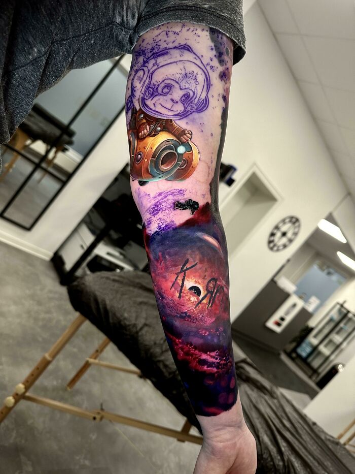 Colorful space-themed tattoo featuring an astronaut and cosmic swirl on a person's forearm, showcasing artistic designs.