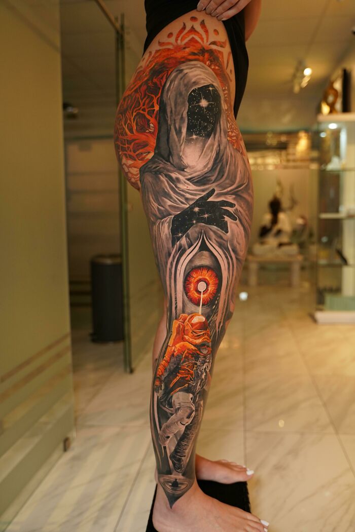 Intricate leg tattoo featuring a cosmic hooded figure with vibrant colors, showcasing exceptional tattoo artist design.