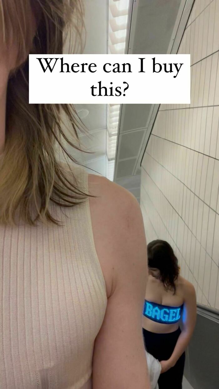 Close-up of a woman on an escalator with a humorous LED sign reading BAGEL, a relatable meme moment.