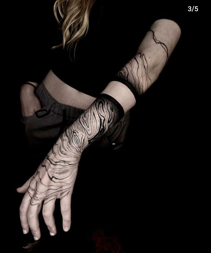 Tattoo artist creates intricate black linework design on a person's arm, showcasing exceptional tattoo craftsmanship.