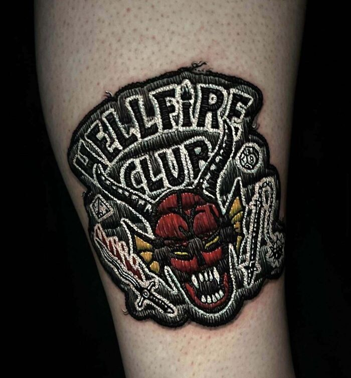 Intricate tattoo design featuring a detailed Hellfire Club patch with bold colors and fine embroidery effects.
