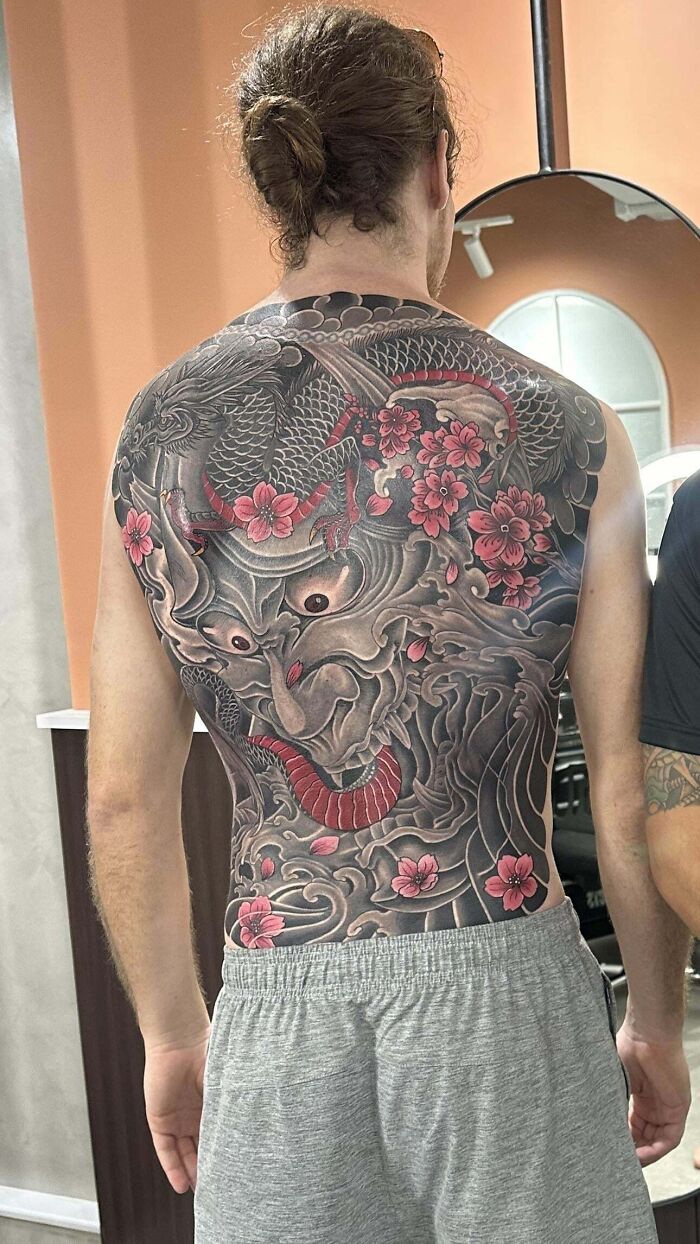 Intricate back tattoo design featuring Japanese motifs and pink cherry blossoms, showcasing a tattoo artist's creativity.