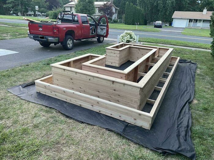 Confusing construction layout with wooden frames on grass, resembling a multi-level platform near a red pickup truck.