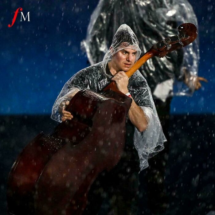 A Cellist In The French National Orchestra Protects His Instrument From The Rain During The Olympics Opening Ceremony