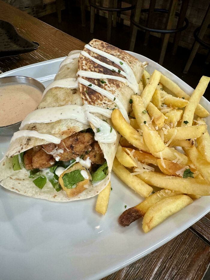 Wrap and fries on a plate with dipping sauce; unique food combination.