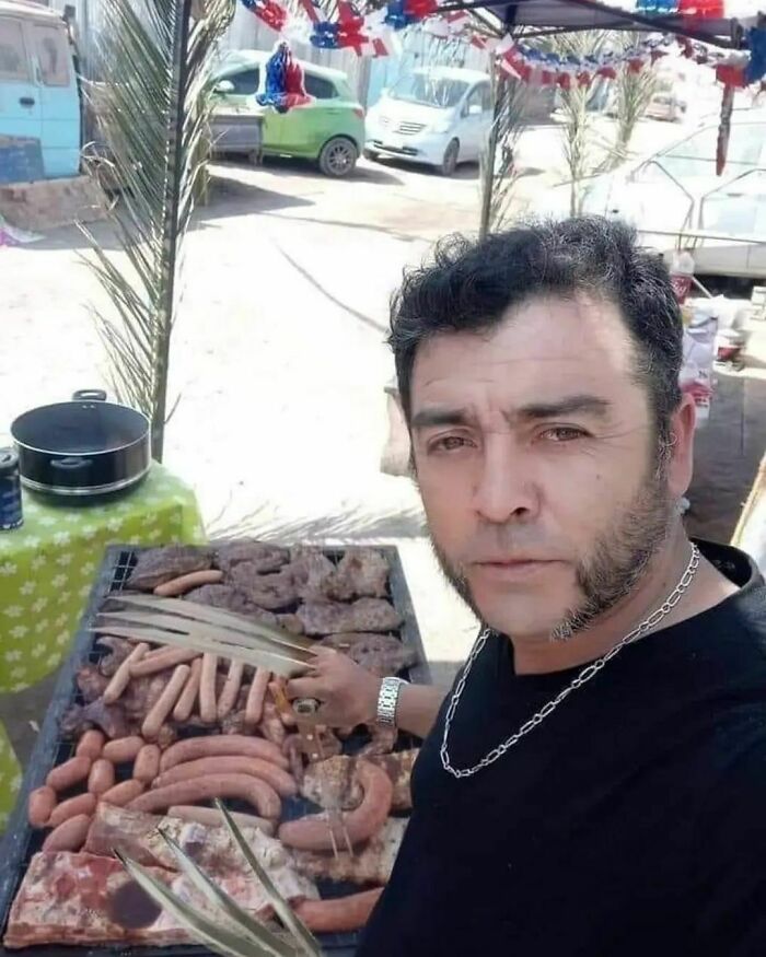 Man grilling various sausages and meat at an outdoor barbecue.