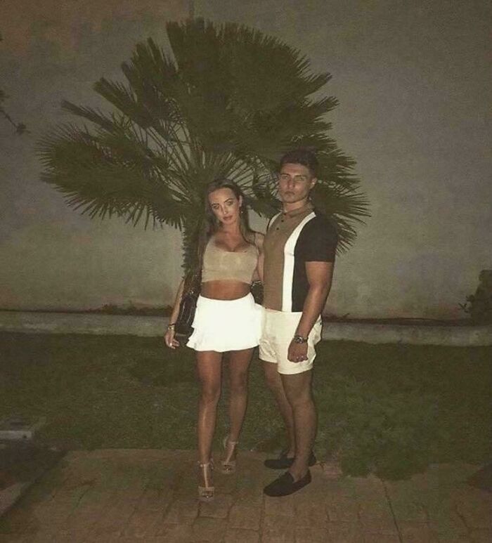 A couple posing in front of a palm tree, creating a confusing optical illusion with their outfits.