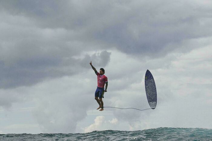 Man appears to float above the ocean next to an upright surfboard, creating a seriously confusing optical illusion.