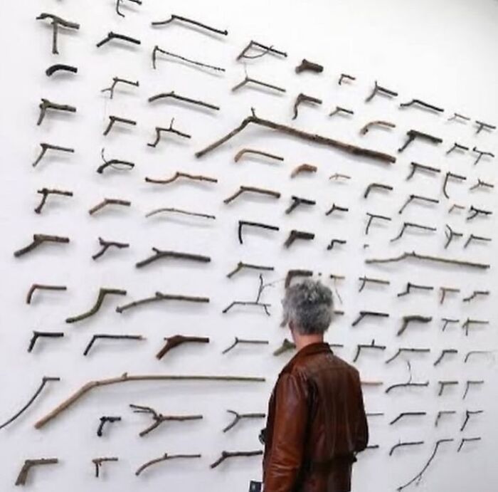 Person in brown jacket observes various stick formations on a gallery wall, emphasizing creativity and artistic expression.