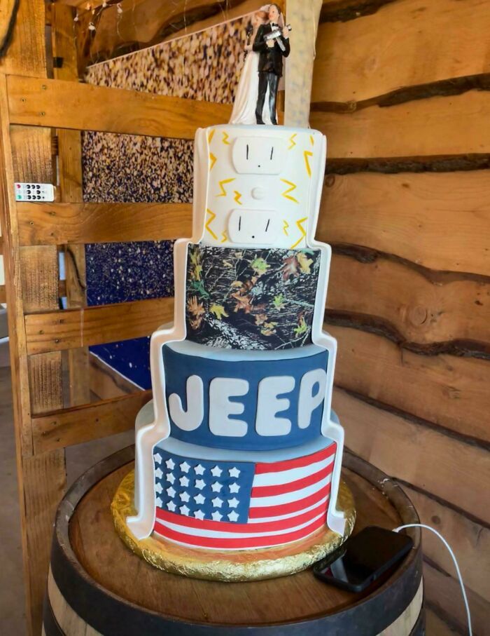 Unconventional wedding cake with Jeep and American flag design topped by a bride and groom figurine.