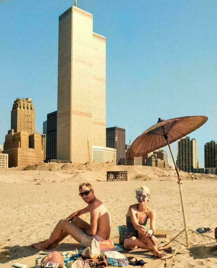 Couple sunbathing on a sandy beach with iconic NYC skyline in the background, capturing a new perspective on famous places.