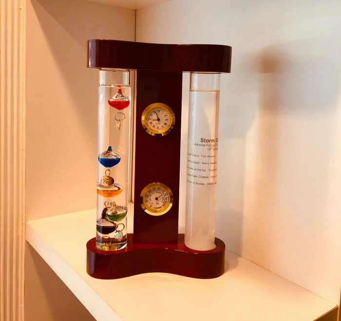 Unique barometer with colorful floats and temperature gauges displayed on a shelf.
