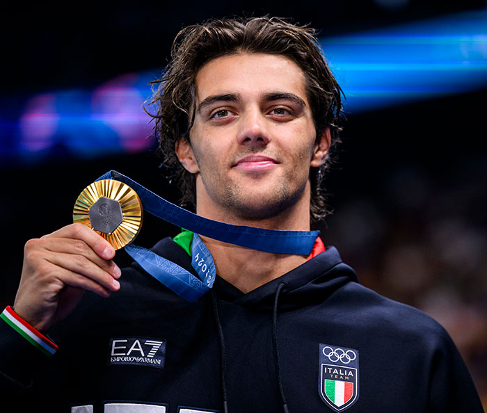 Gold medalist in black hoodie holding medal at an event.