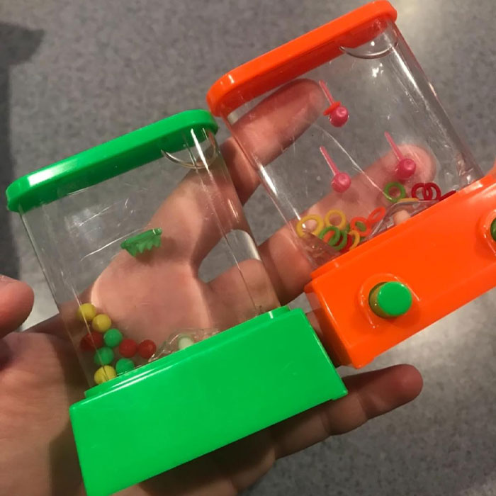 Hand holding two mini water ring toss games with colorful buttons and pegs; a fun and ridiculous find.