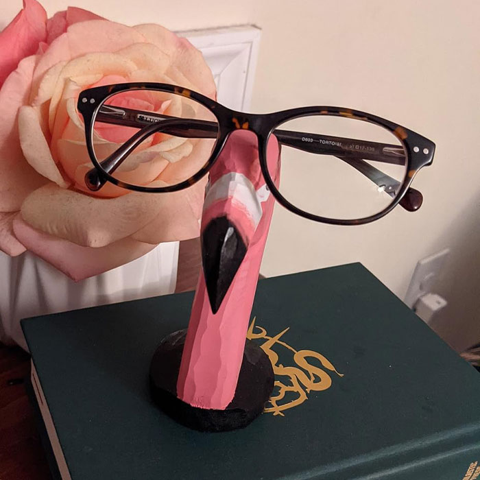 Quirky flamingo glasses holder on a book with a rose in the background, showcasing ridiculous finds.