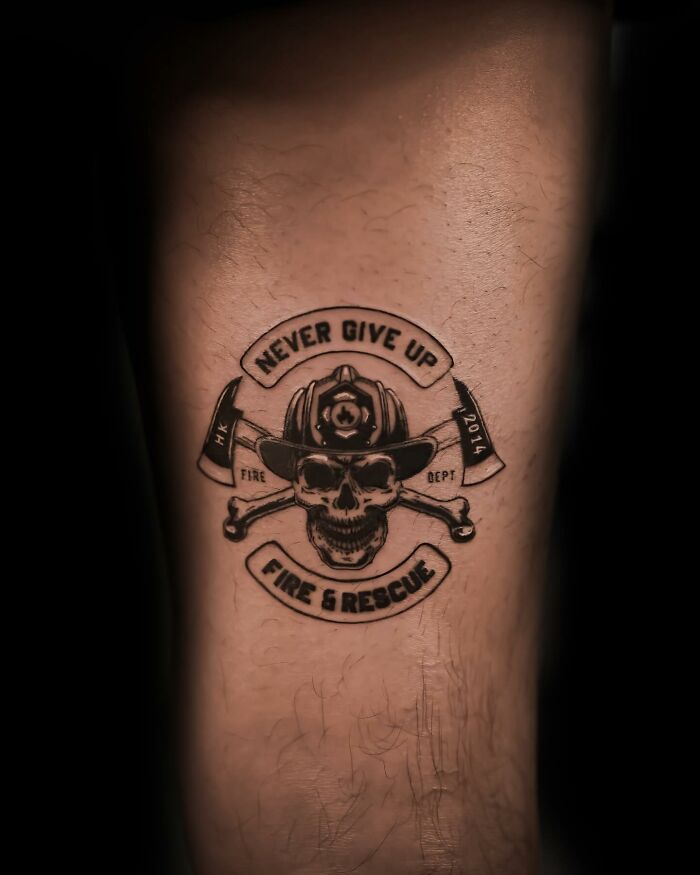 Hyperrealistic tattoo of a firefighter helmet with skull and axes, featuring the words "Never Give Up" and "Fire & Rescue".