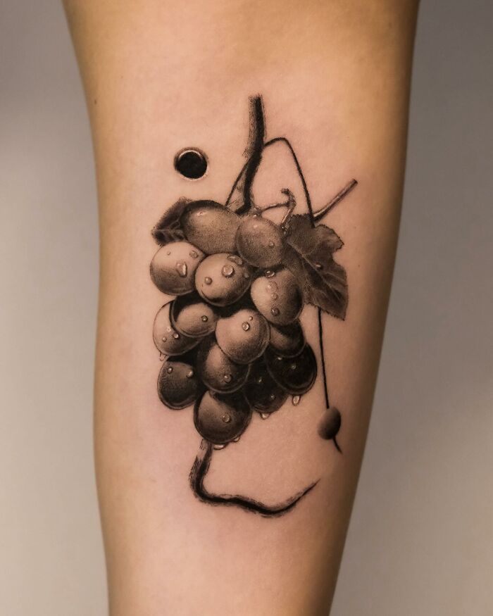 Hyperrealistic tattoo of grapes on skin, showcasing detailed artwork resembling a photograph.