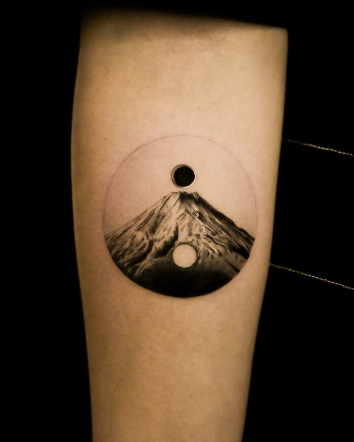 Hyperrealistic tattoo of a mountain within a yin-yang circle on a person's forearm.