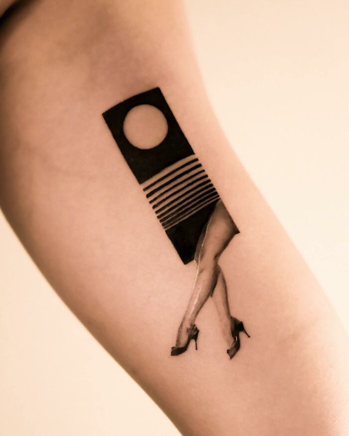 Hyperrealistic tattoo on arm, depicting a woman's legs in high heels emerging from a geometric design.