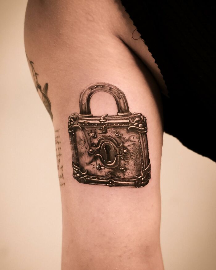 Hyperrealistic tattoo of a vintage padlock on an arm, showcasing intricate detail and lifelike shading.