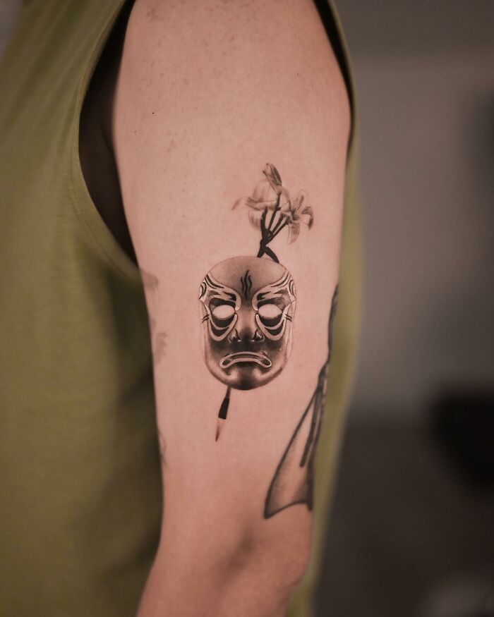 Hyperrealistic tattoo of a detailed mask on a person's arm.
