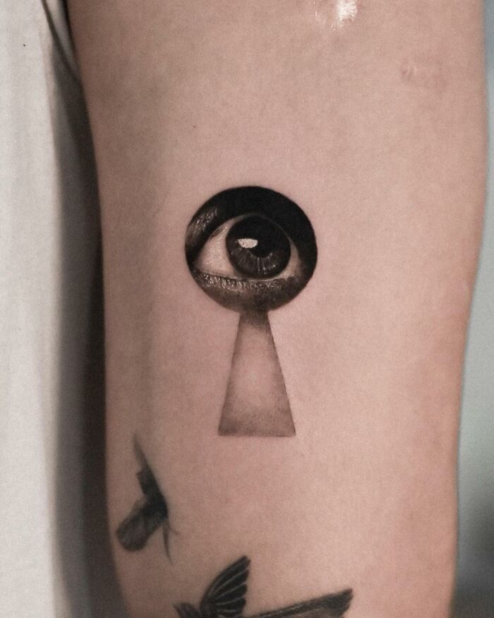 Hyperrealistic tattoo of an eye inside a keyhole on an arm, showcasing detailed artistry.