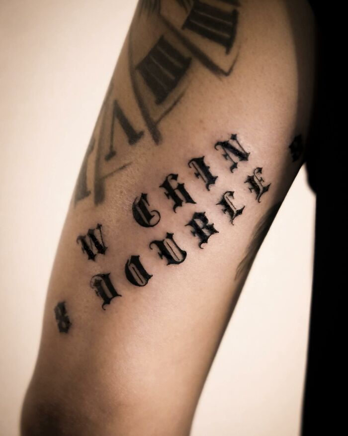 Hyperrealistic tattoo on arm featuring bold, black lettering and clock design, resembling a detailed photograph.