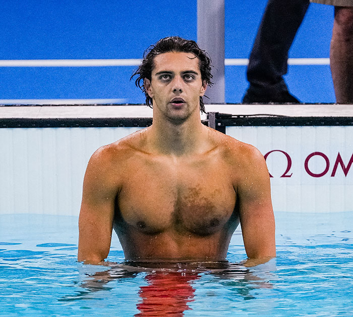 Gold medalist swimmer standing in the pool after a race, facing the camera.