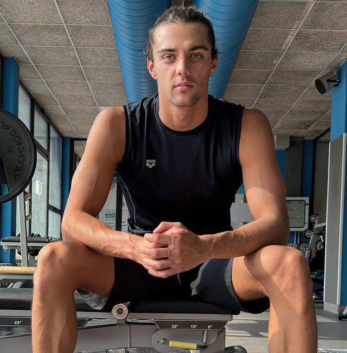 Gold medalist Thomas Ceccon seated in a gym wearing a black tank top, looking at the camera.
