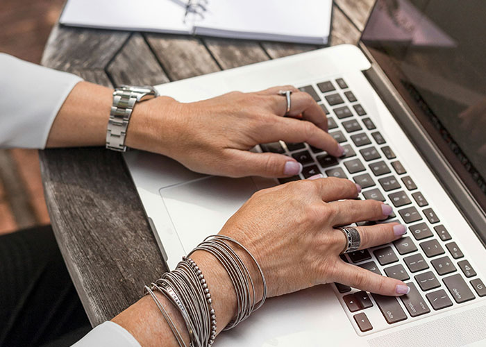 Hands with bracelets typing on a laptop keyboard, illustrating workplace errors and colossal mess-ups at work.