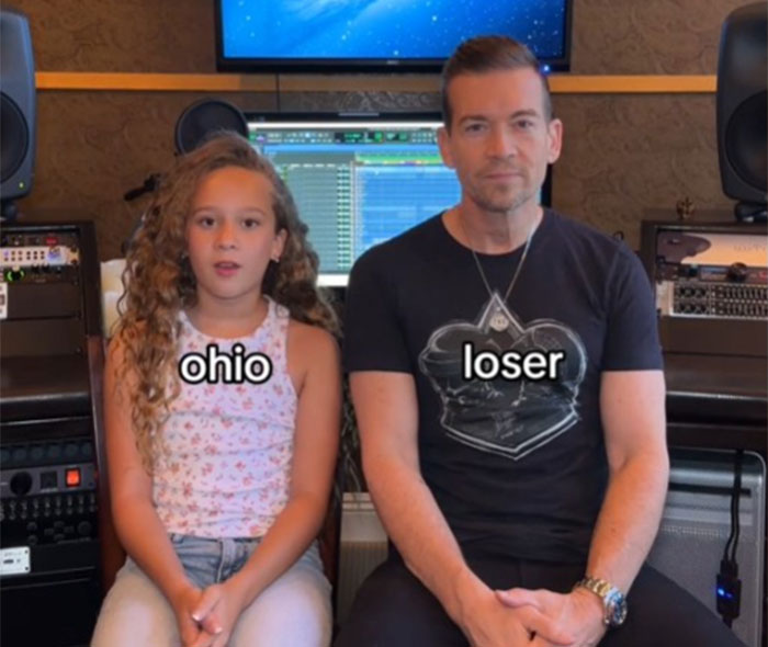 Father learning slang from daughter, seated together in a studio, with screens and speakers in the background.