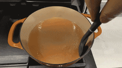 Hand stirring water boiling in an orange pot, demonstrating kitchen items that tackle common kitchen problems efficiently.